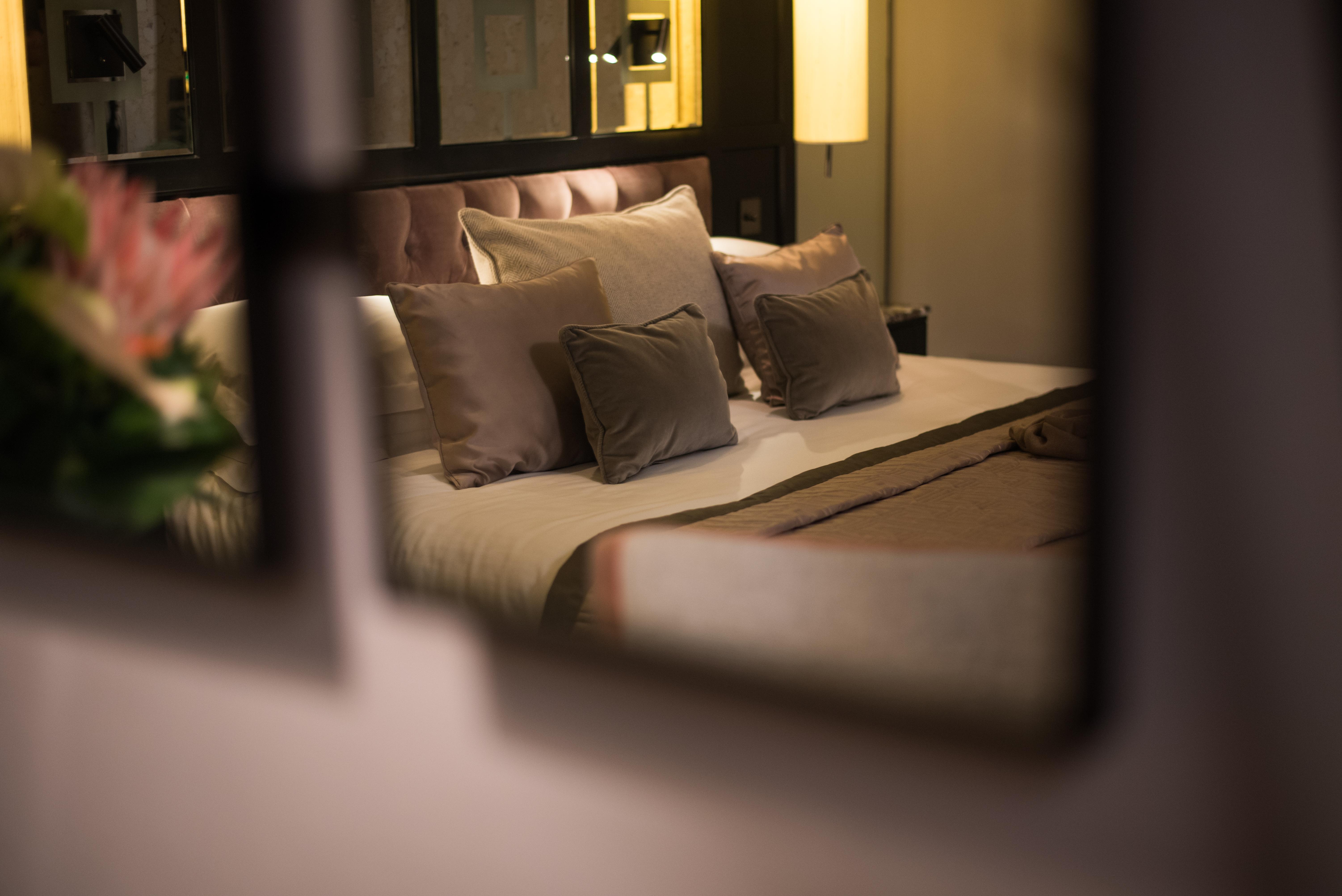 The Fitzwilliam Hotel Belfast Kültér fotó The photo shows a cozy and elegantly decorated bedroom. The focal point is a plush bed with soft, neutral-colored bedding and several decorative pillows arranged neatly on it. The room has a warm ambiance, enhanced by a standing lamp that provides so