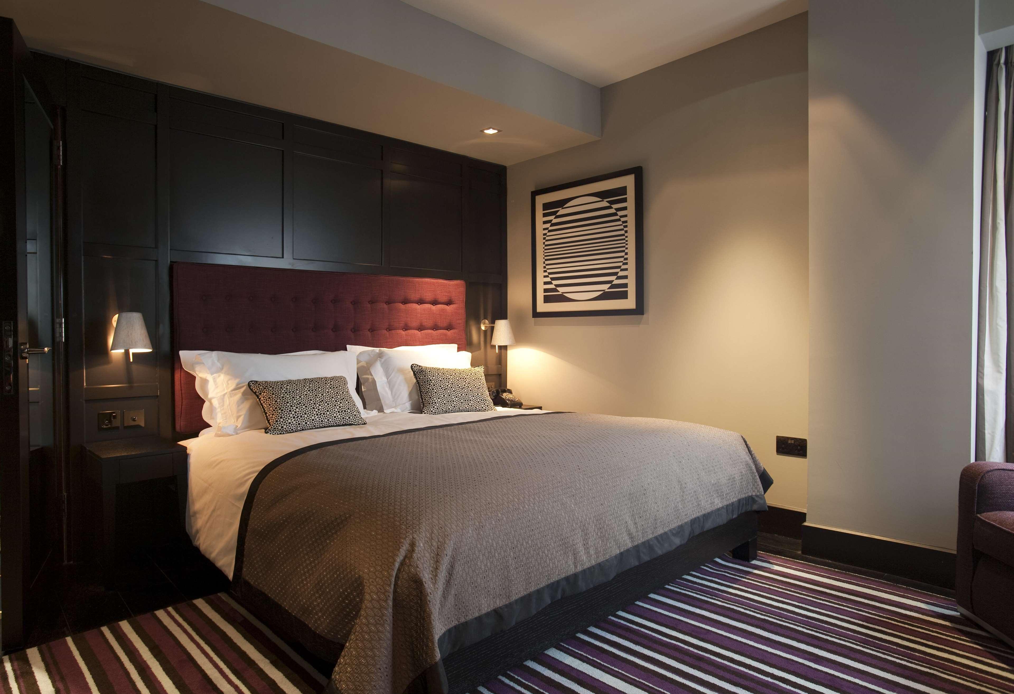 The Fitzwilliam Hotel Belfast Kültér fotó The photo shows a stylish and modern hotel room. It features a large bed with a tufted headboard in a deep burgundy color. The bed is dressed with neutral-toned bedding and decorative pillows. On either side of the bed, there are small bedside lamps 