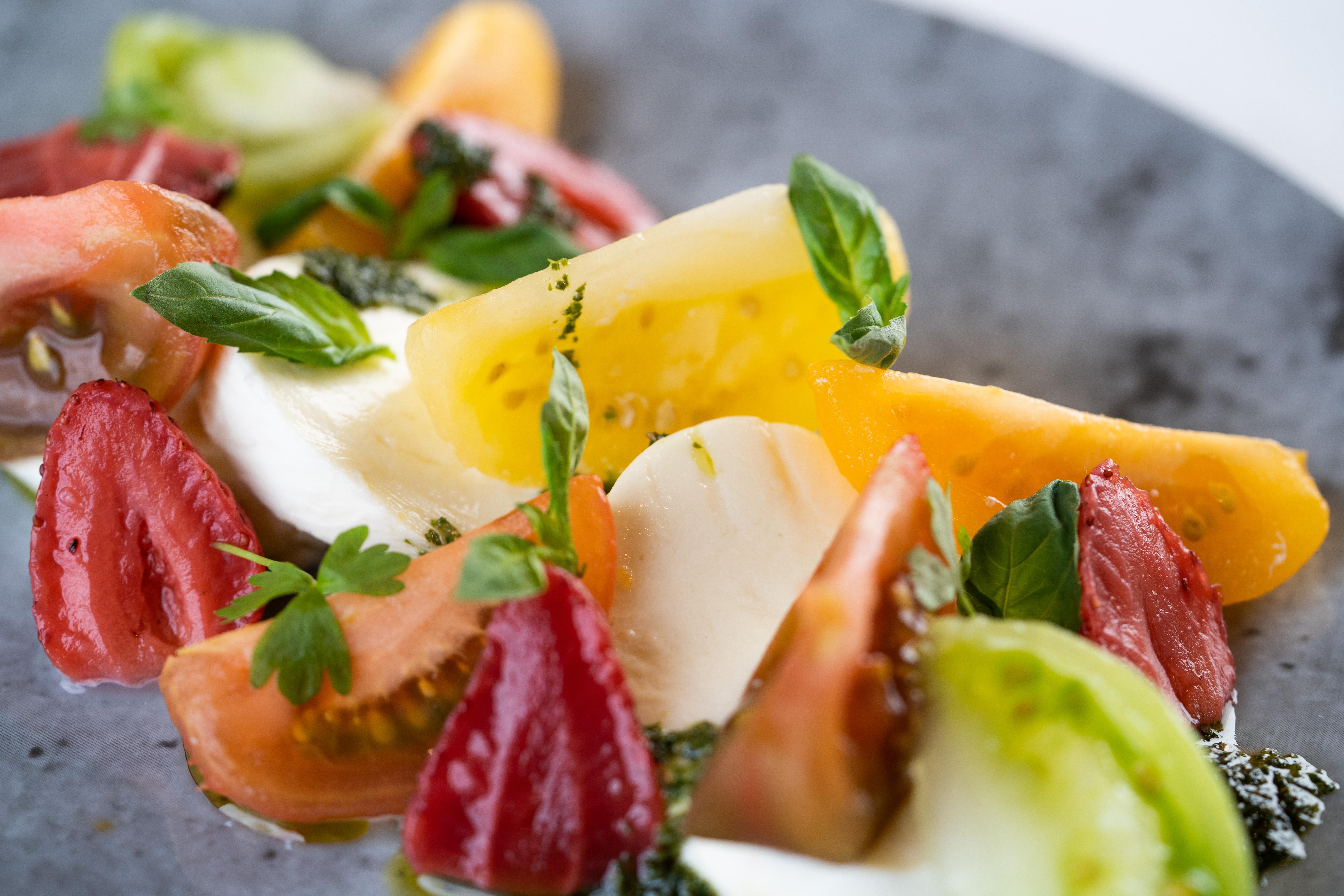 The Fitzwilliam Hotel Belfast Kültér fotó The photo shows a vibrant salad featuring slices of various tomatoes, including red, yellow, and green varieties. The tomatoes are paired with fresh mozzarella cheese and garnished with basil leaves. The dish is presented on a round, dark plate, high