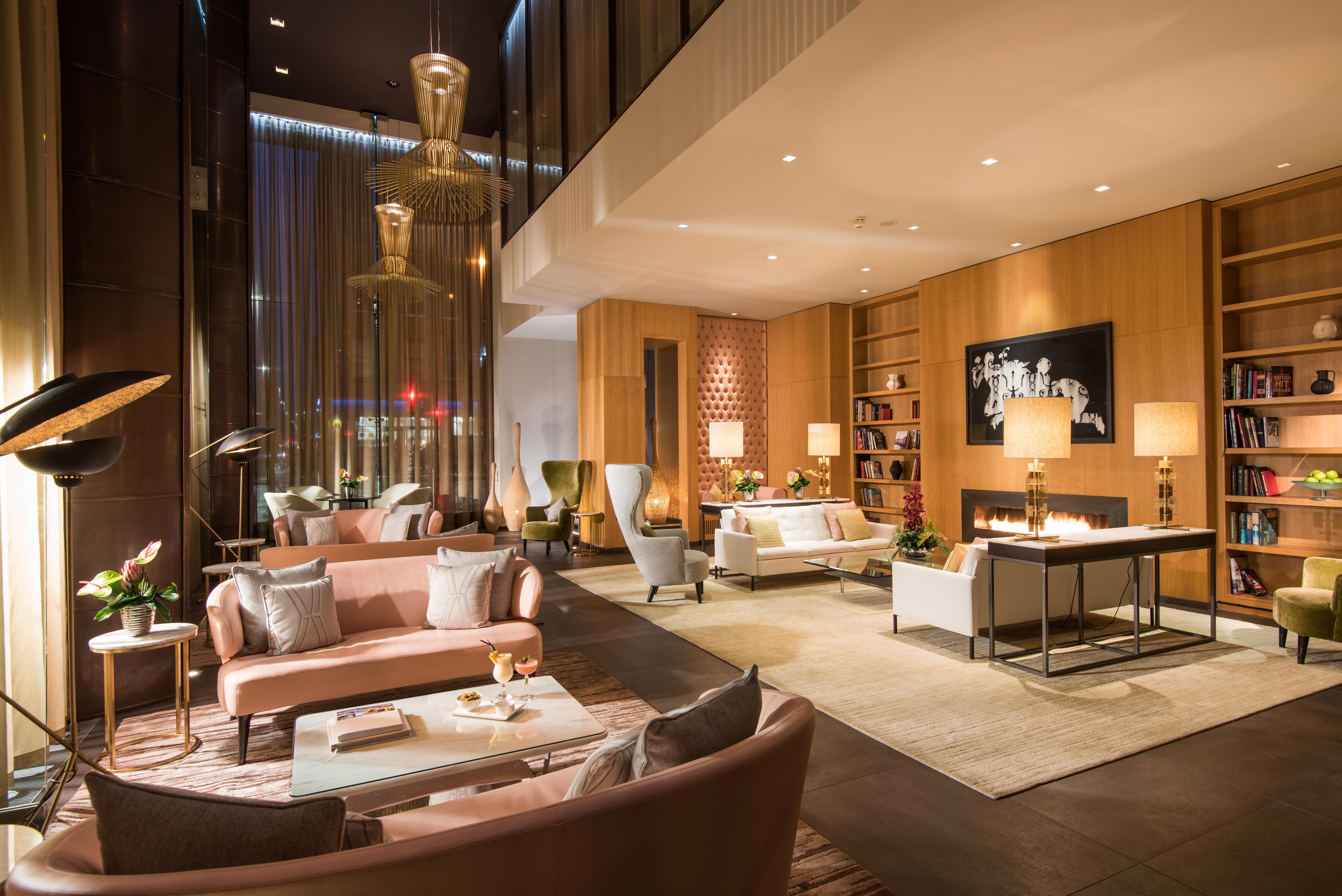 The Fitzwilliam Hotel Belfast Kültér fotó The photo shows a modern and elegant lobby or lounge area. The space features a mix of contemporary and cozy furniture, including light-colored sofas and armchairs arranged around small tables. There are decorative elements like vases with flowers, a
